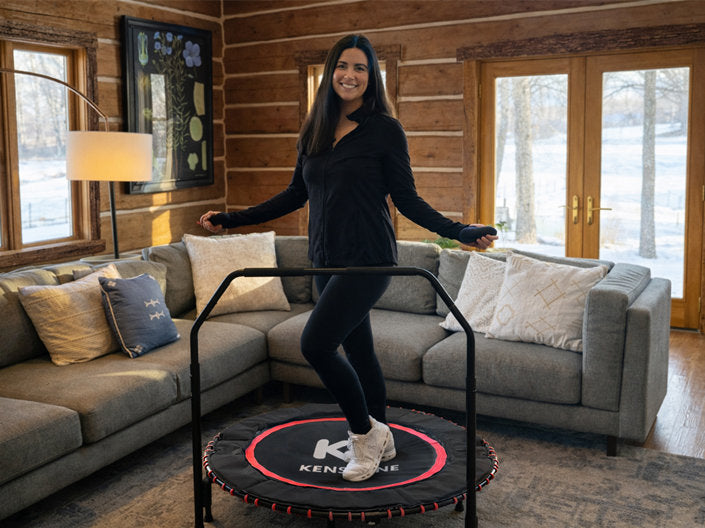 Woman jumping on a trampoline in a living room with wooden walls and large windows.